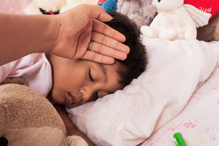 niño enfermo en cama con fiebre, la madre lo revisa